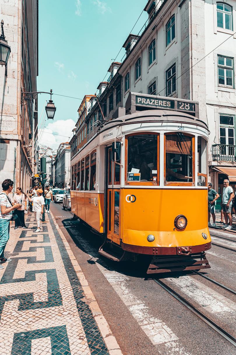 A typical yellow and white tram on a Lisbon street during daytime