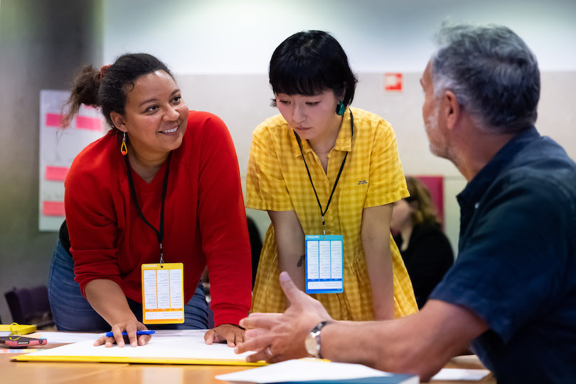 Three attendees collaborating in a workshop exercise at UXLx