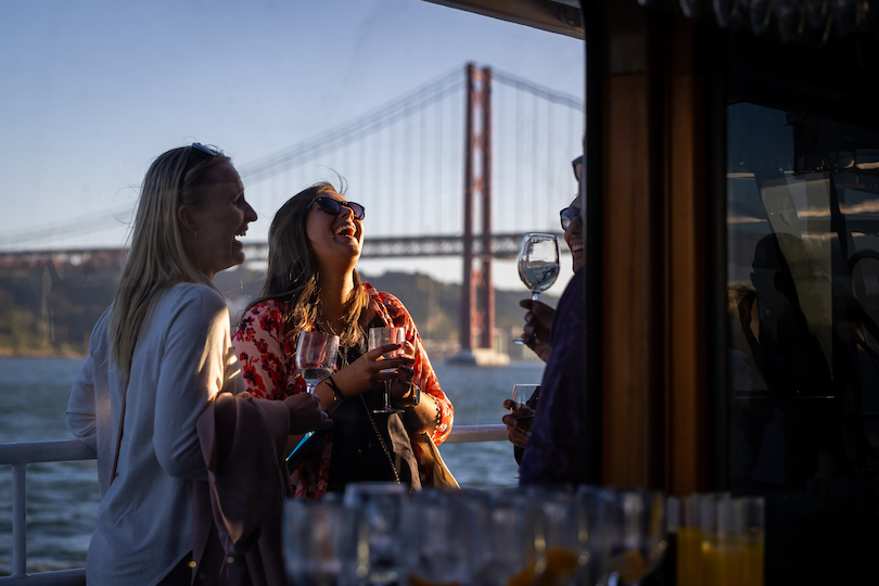 Attendees laughing and holding glasses of wine at the sunset cruise party of UXLx 2024